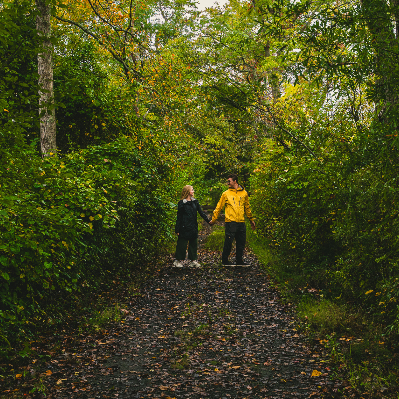 Jordyn and JT holding hands in the center of the frame with trees behind them.