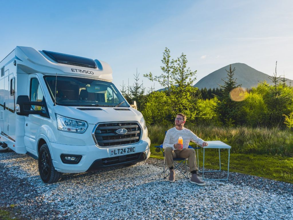 JT sitting at a table next to our motorhome on our scottish highlands road trip. you can see the mountains in the background.