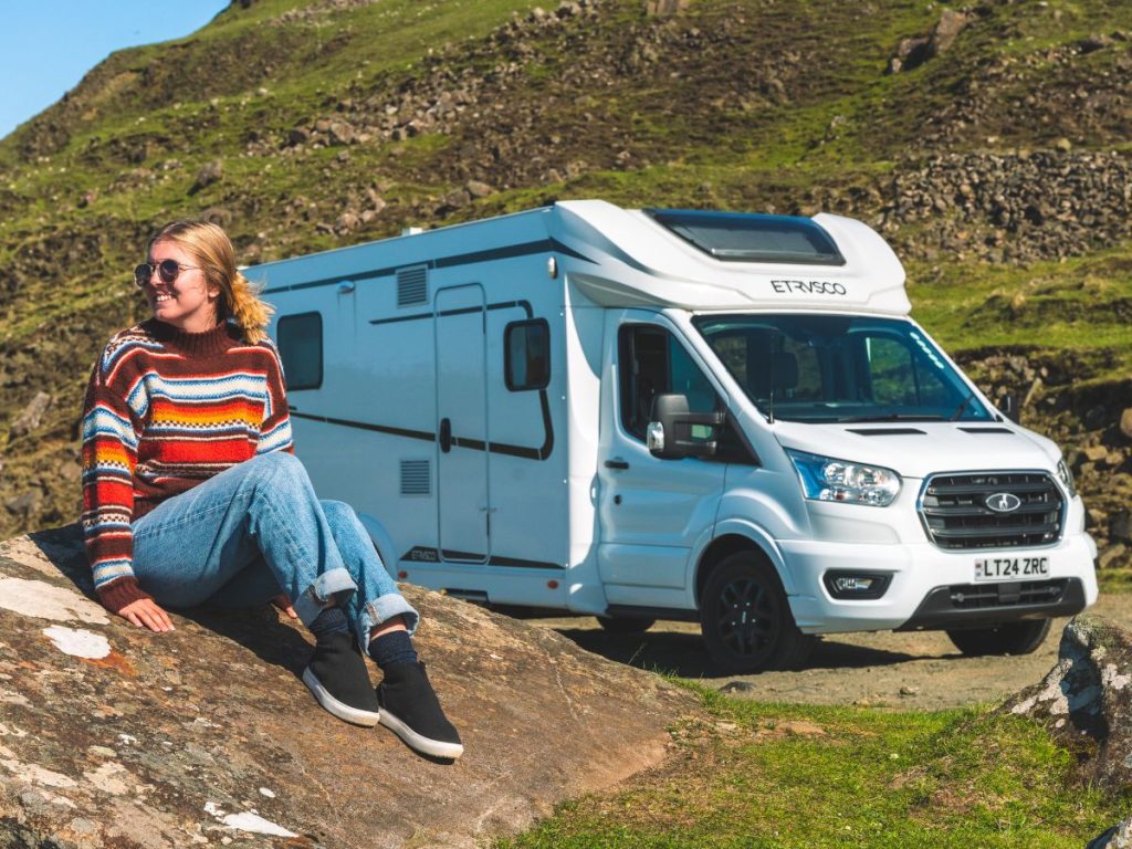 Me sitting on a rock next to the motorhome on our Me hanging outside of the motorhome that we rented for our Scottish Highlands Road Trip.