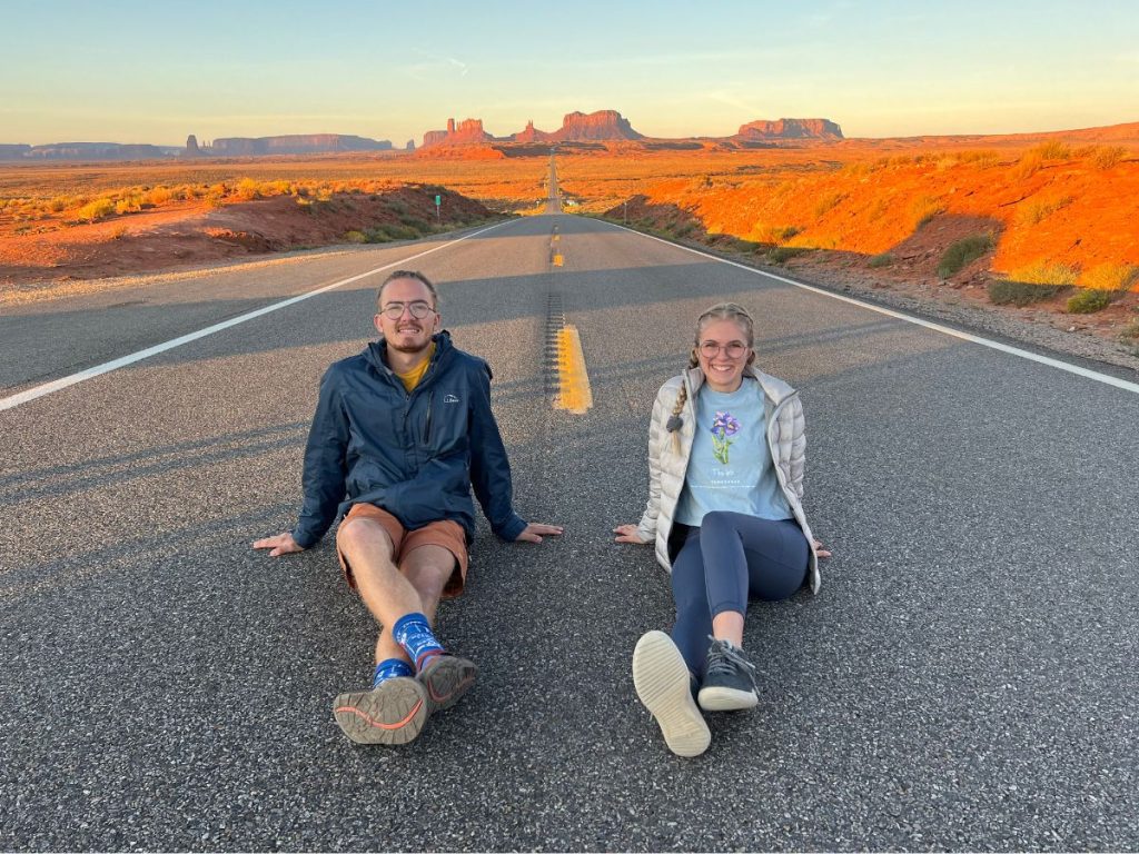 Jordyn and JT sitting in the middle of the road with monument valley in the background.