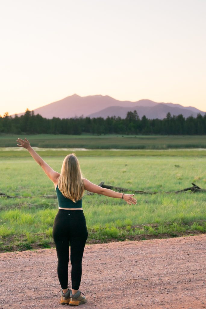 Jordyn standing in the pines with mount humphreys behind her on her arizona road trip