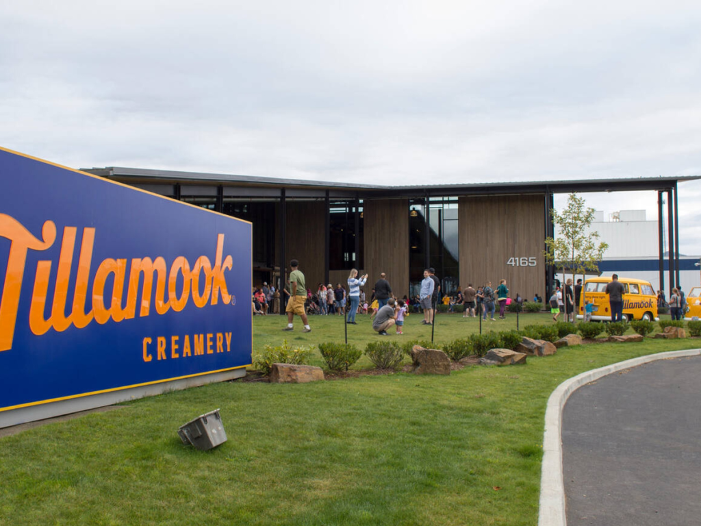 Visitors gathered outside the Tillamook Creamery in Oregon, with a large blue and orange sign and classic yellow Tillamook vans, a popular food stop on a Pacific Northwest road trip.
