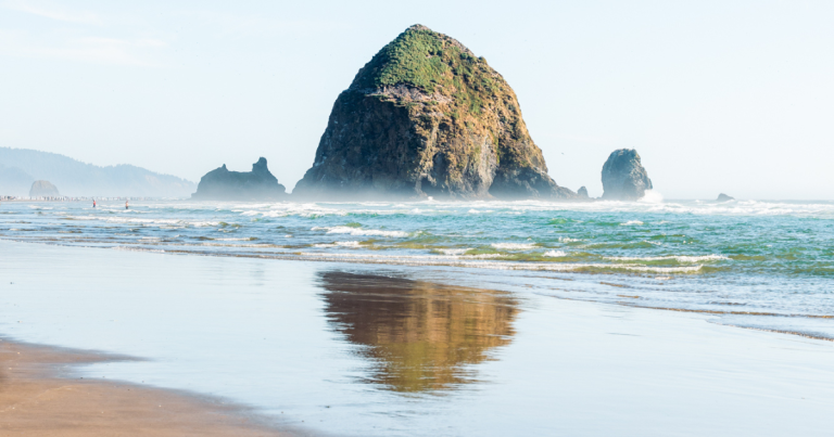 Haystack Rock reflecting in the wet sand at low tide on Cannon Beach, a must-see stop along the Pacific Northwest road trip coastline.