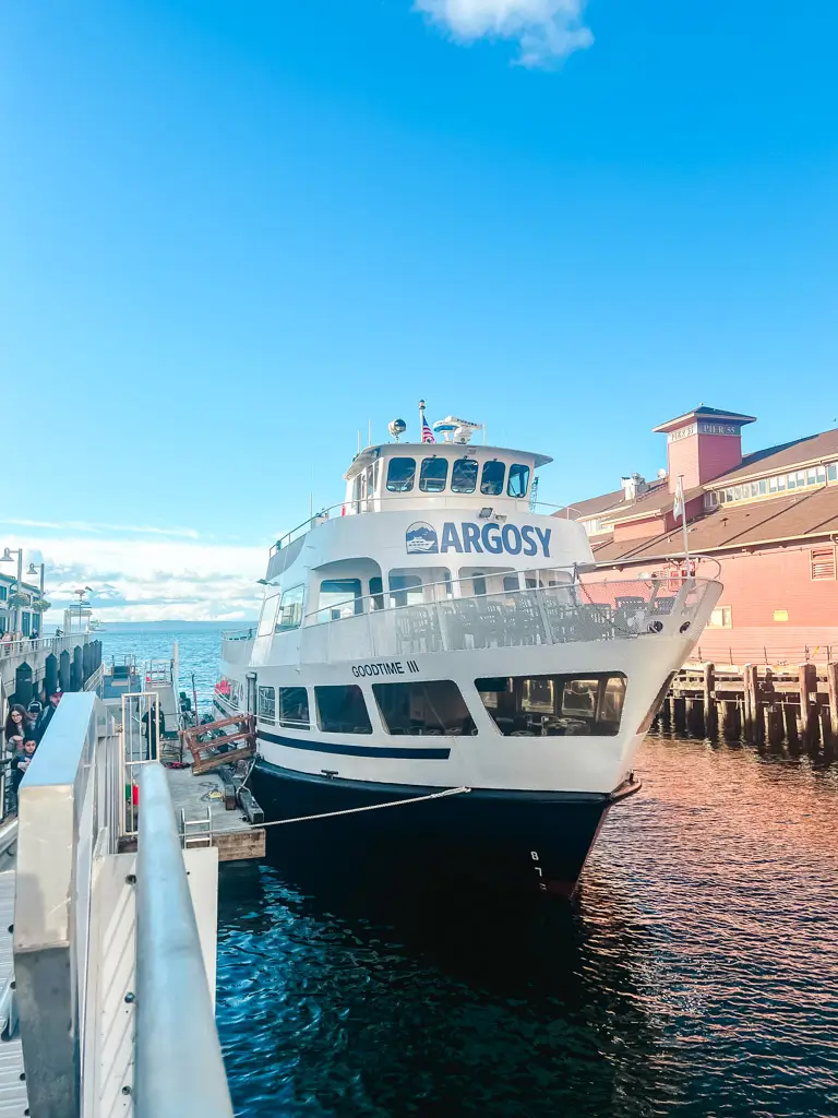 An Argosy Cruises sightseeing boat docked along Seattle's waterfront near Pier 55, ready for a harbor cruise across Elliott Bay with the city's historic waterfront in the background.