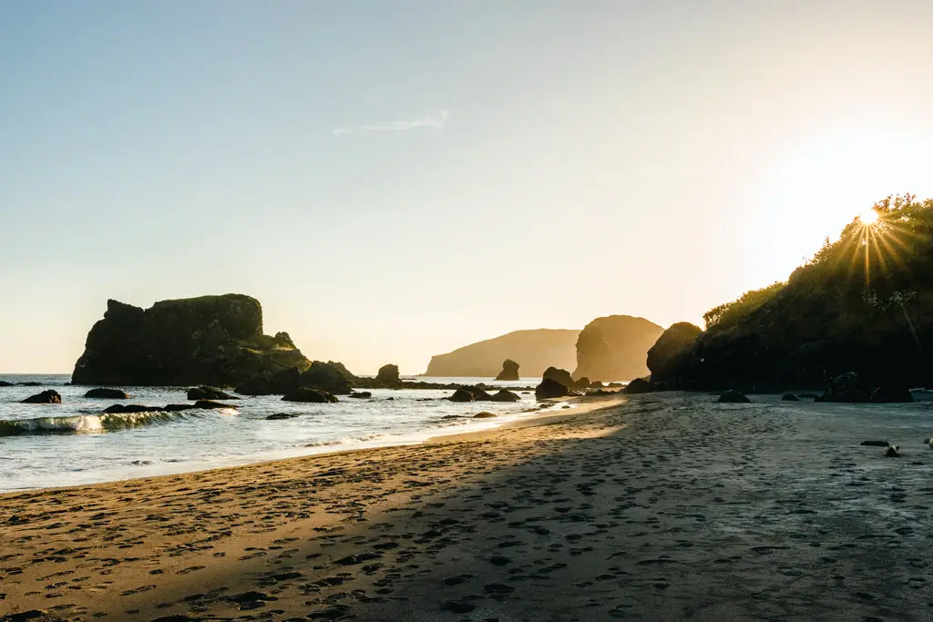 Golden sunset over the sandy shoreline at Harris Beach State Park, with rugged sea stacks, gentle ocean waves, and dramatic rock formations along the Southern Oregon Coast.
