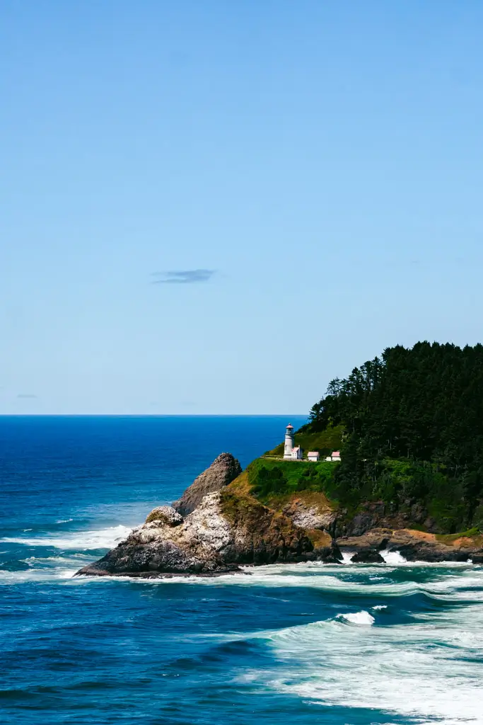 Heceta Head Lighthouse perched on a rugged cliff overlooking the Pacific Ocean, surrounded by evergreen forest and dramatic coastal waves along the Oregon Coast.