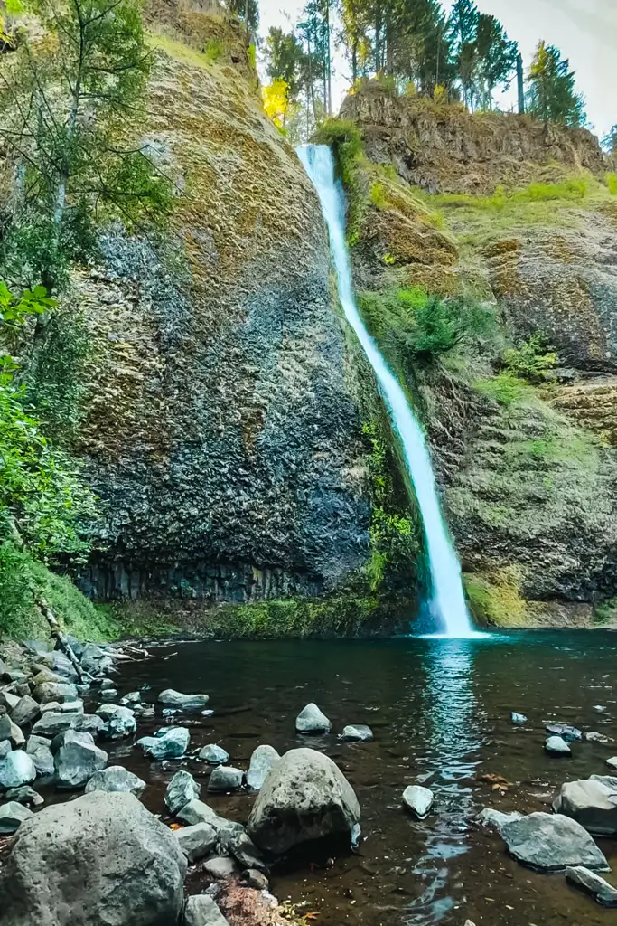 Horsetail Falls cascading down a tall basalt cliff into a clear pool surrounded by moss-covered rocks and lush forest in the Columbia River Gorge, Oregon.