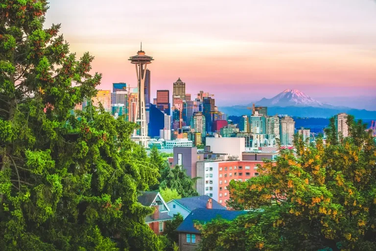 Seattle's skyline viewed from Kerry Park at sunset, featuring the iconic Space Needle with Mount Rainier rising in the distance beneath colorful evening skies.