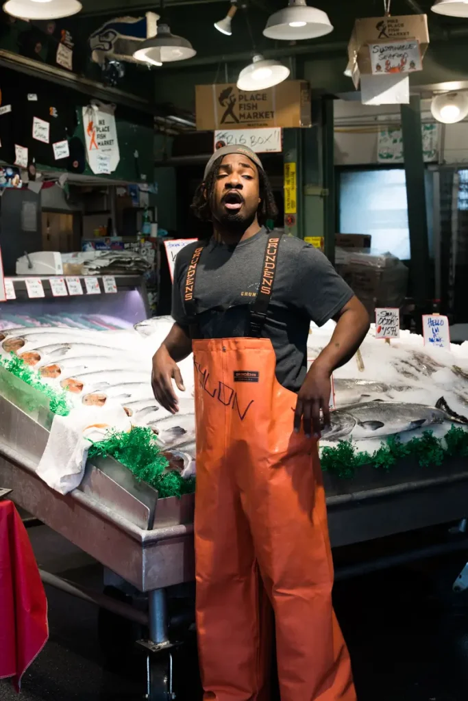 A fishmonger standing behind a display of fresh seafood at Pike Place Fish Market in Seattle, Washington, where the market is famous for its iconic flying fish tradition.