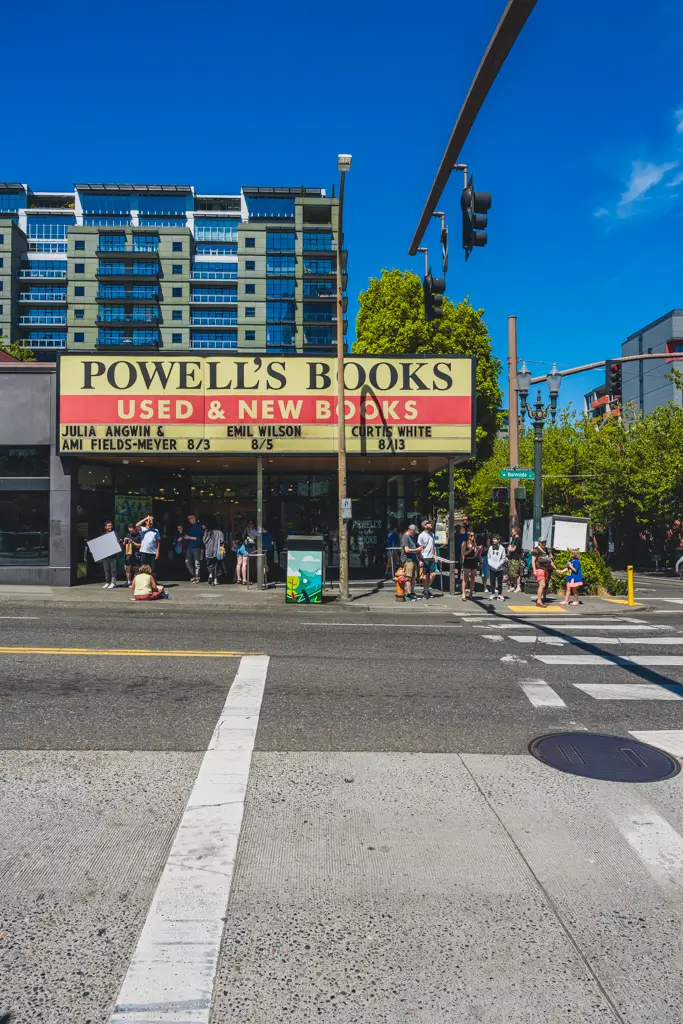 Exterior of Powell’s Books in downtown Portland, Oregon, with the Used & New Books marquee, pedestrians gathered outside, and a bright blue summer sky.