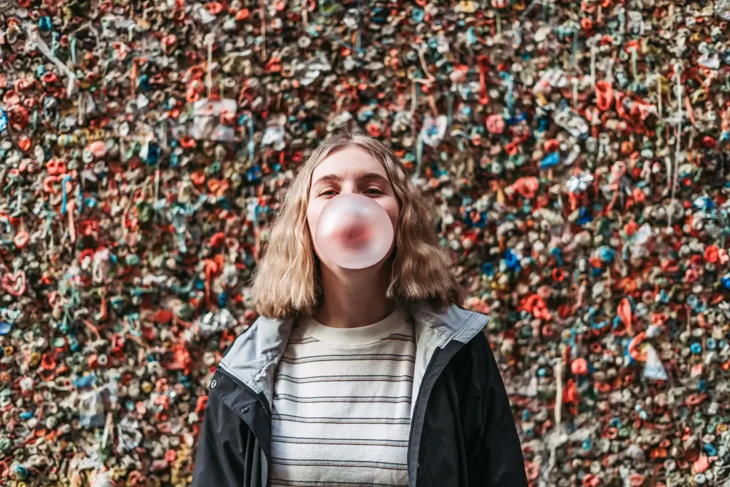 A traveler blows a bubble with gum while standing in front of the colorful Seattle Gum Wall near Pike Place Market in downtown Seattle, Washington.