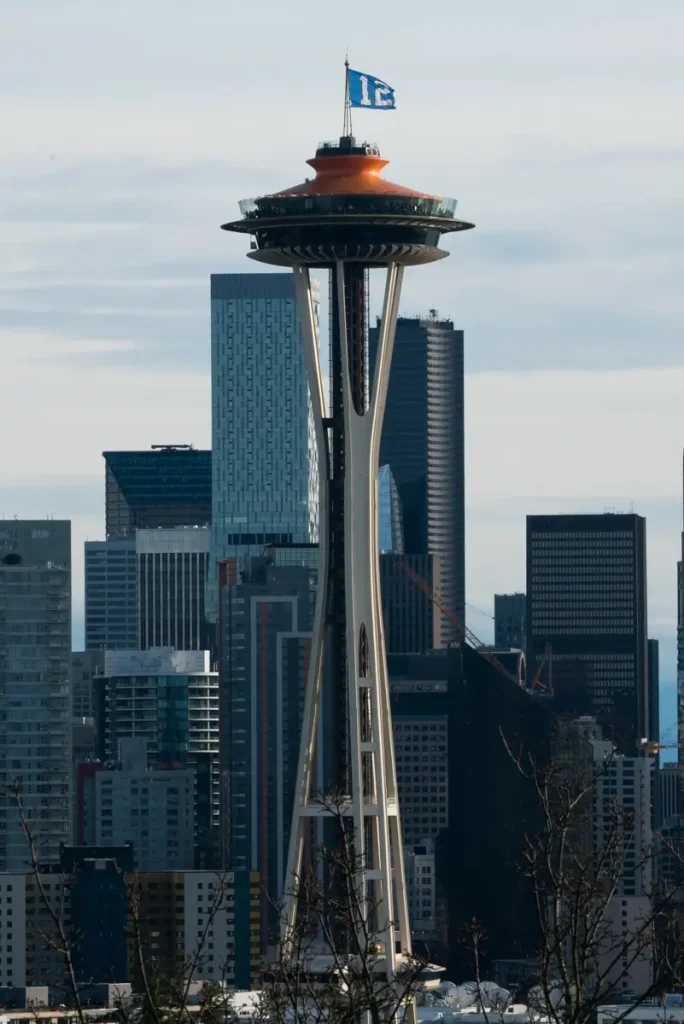 The Space Needle rising above downtown Seattle's skyline, with the city's skyscrapers in the background and the iconic 12 flag flying atop the observation tower.