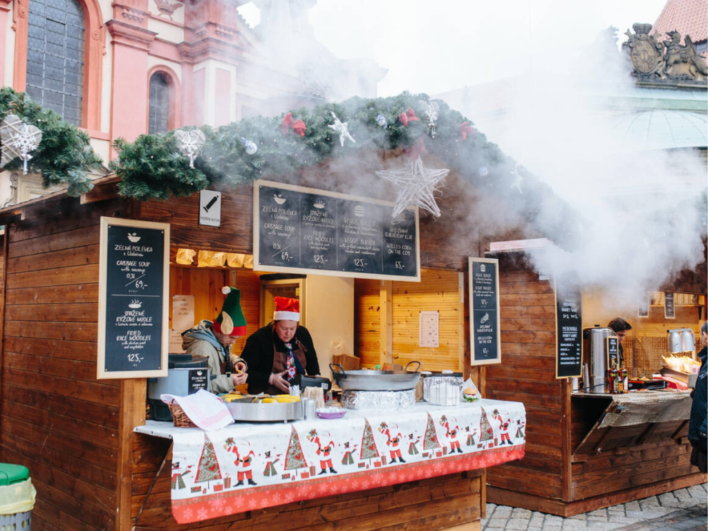 Steam rising from festive wooden food stalls at the Christmas markets in Bratislava, with garlands, holiday decor, and traditional Slovak dishes being served.