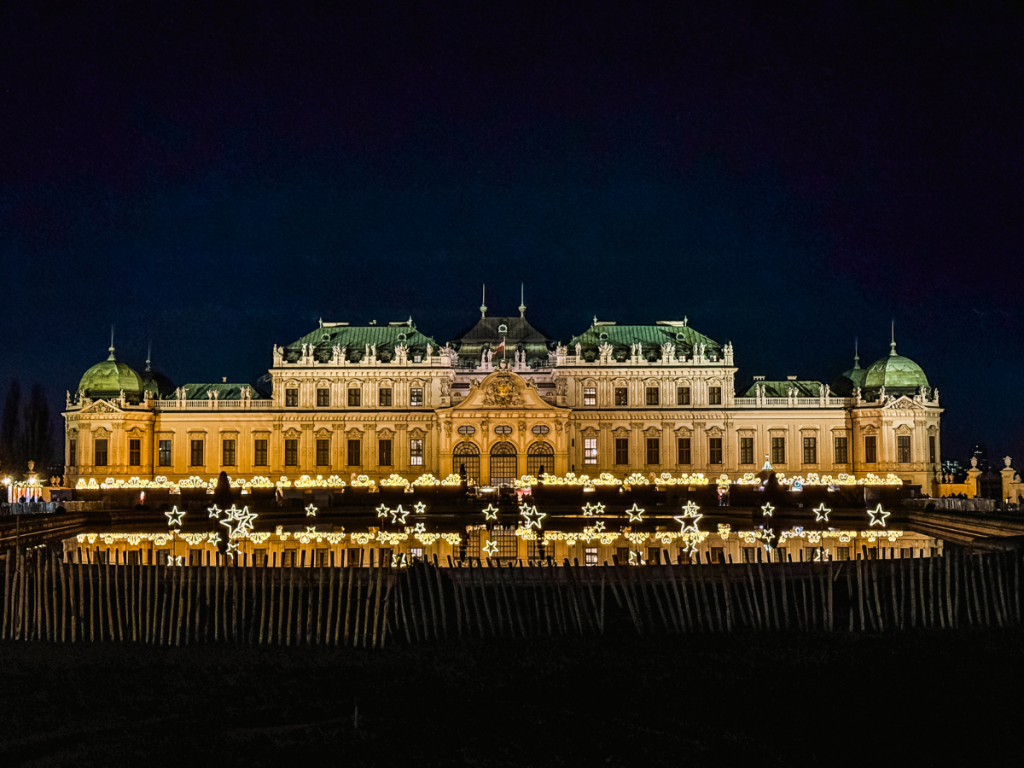 Belvedere Palace in Vienna glowing under night skies with festive star-shaped lights reflecting in the water, marking the elegant setting of one of the city’s most magical Christmas markets.