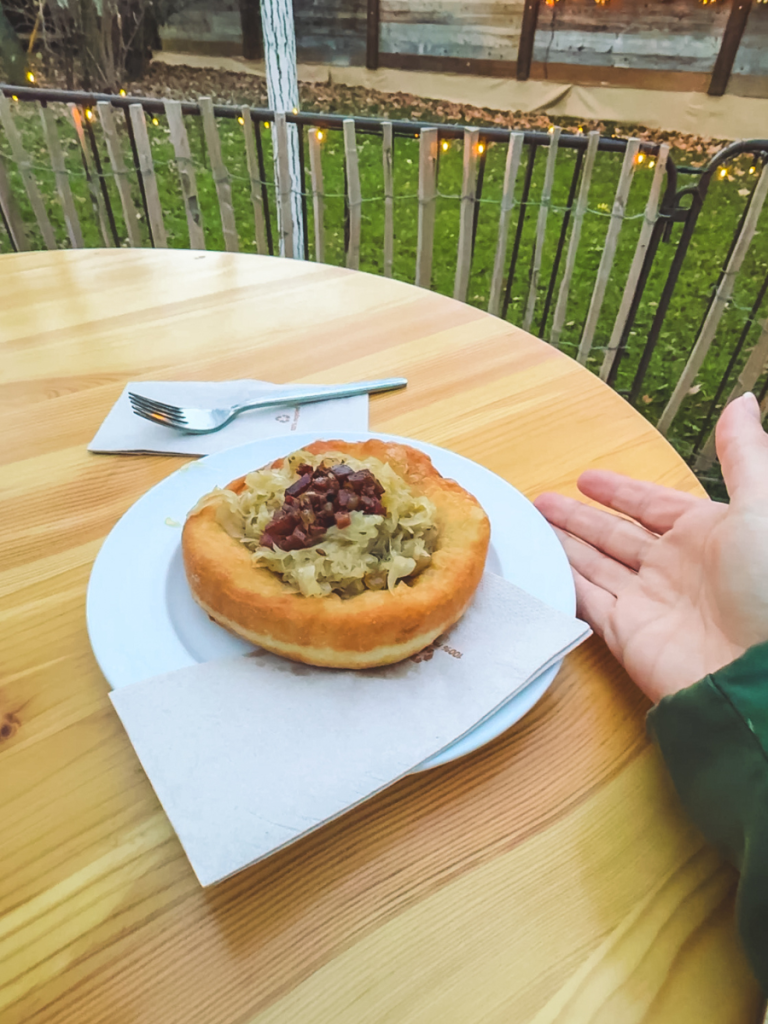 A plate of freshly made Langos topped with sauerkraut and crispy bacon served at an outdoor table during Vienna’s Christmas market season.