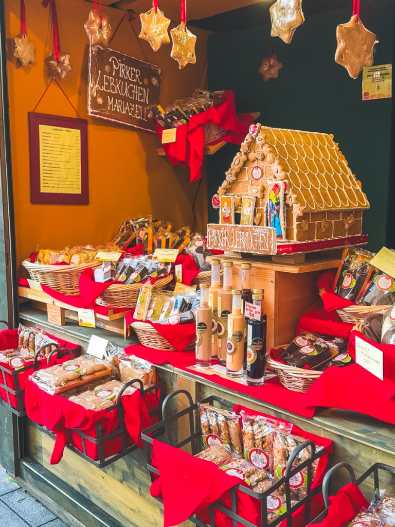 A Christmas market stall in Vienna decorated with gingerbread stars and filled with traditional Austrian Lebkuchen, gingerbread houses, and holiday sweets from Pirker Lebkuchen Mariazell.