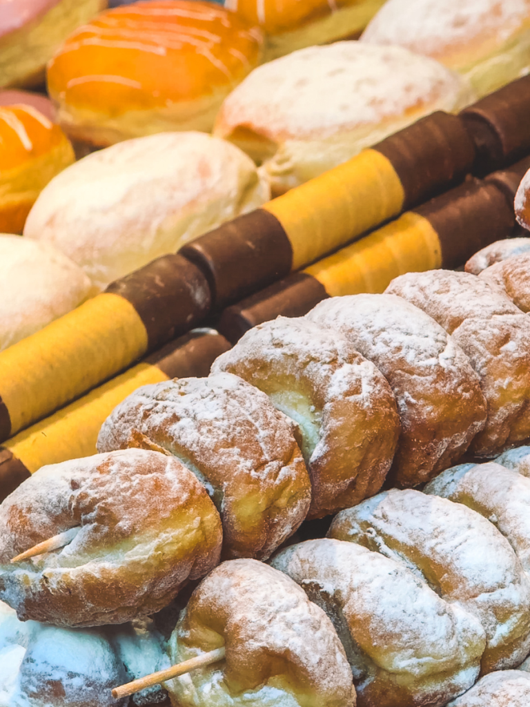 Rows of powdered sugar-dusted pastries, jam-filled donuts, and chimney cakes on display at a Vienna Christmas market food stall.