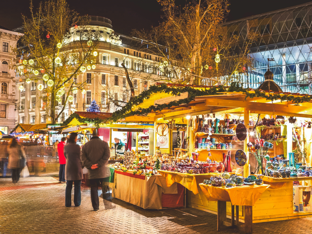 Crowds shopping at a festive Budapest Christmas market with glowing lights, handmade crafts, and decorated wooden stalls at night