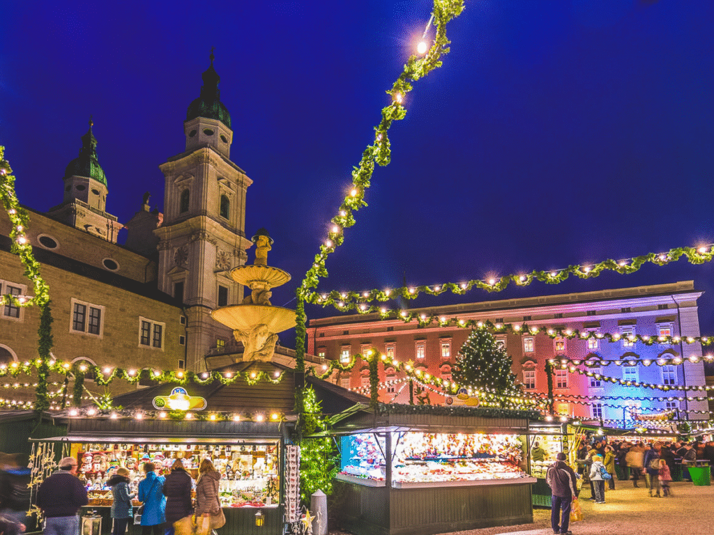 Festive Salzburg Christmas market in a historic square with string lights, decorated stalls, and a cathedral backdrop at night