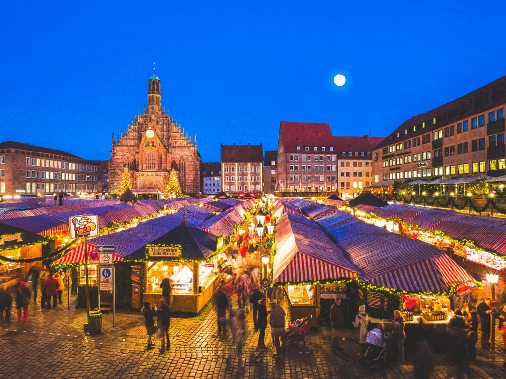 Crowds walking through the Nuremberg Christmas Market in Germany, with striped red-and-white stalls, festive lights, and the Church of Our Lady in the background