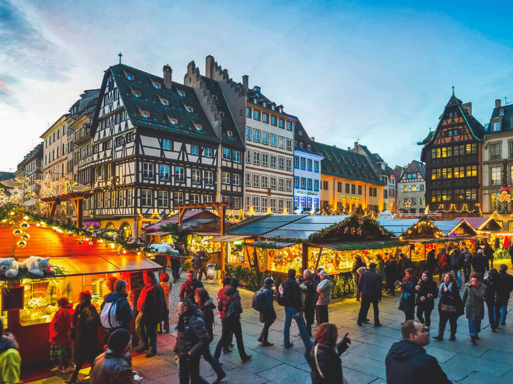 Shoppers exploring Strasbourg’s historic Christmas market in France, with glowing wooden stalls and traditional half-timbered Alsatian buildings in the background