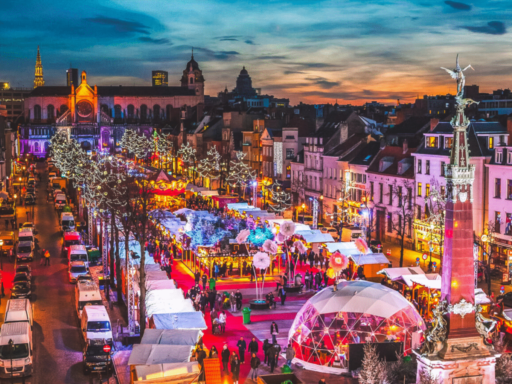 Aerial view of Brussels Winter Wonders Christmas Market in Belgium, with twinkling lights, market stalls, a glowing dome, and Sainte-Catherine Church at dusk