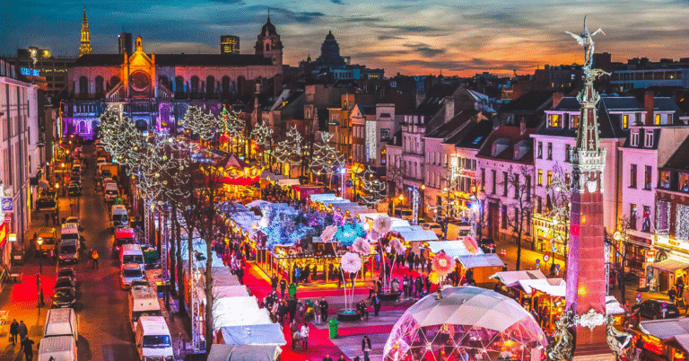 Aerial view of Brussels Winter Wonders Christmas Market in Belgium, with twinkling lights, market stalls, a glowing dome, and Sainte-Catherine Church at dusk