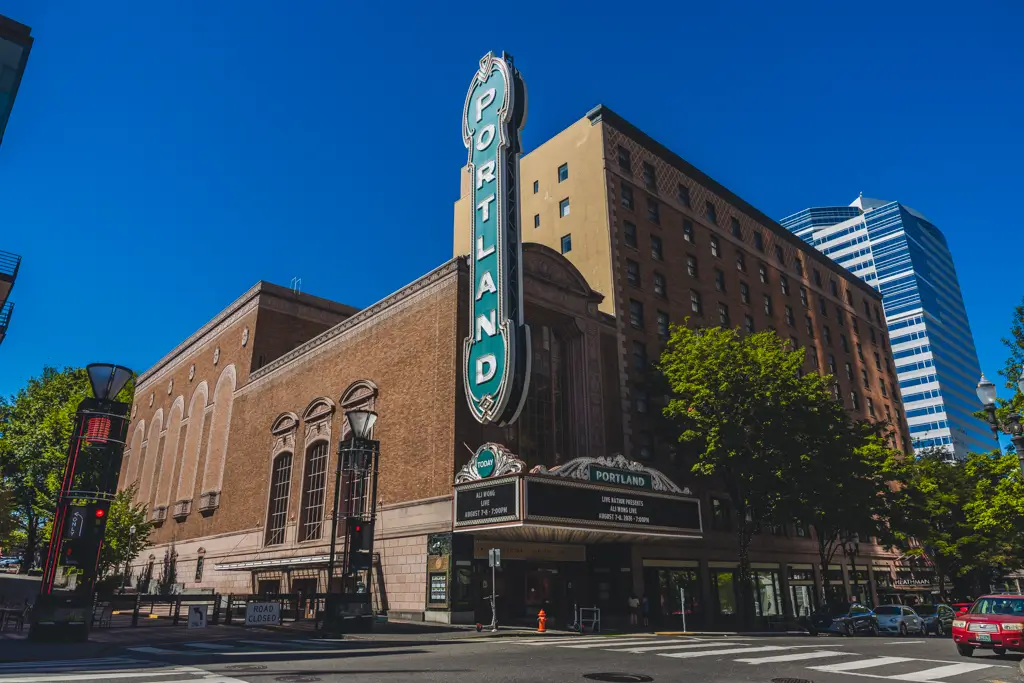 Exterior of the historic Arlene Schnitzer Concert Hall in downtown Portland, Oregon, featuring its iconic vertical Portland sign against a bright blue sky.