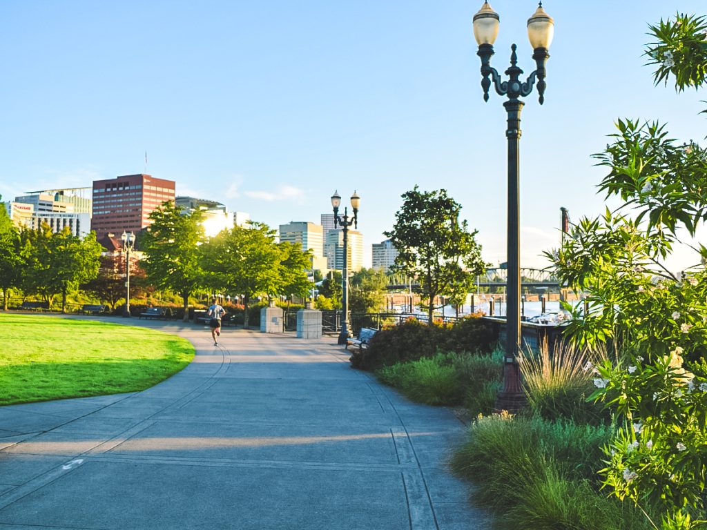Scenic walking path along the Portland waterfront with skyline views, trees, and river on a sunny day