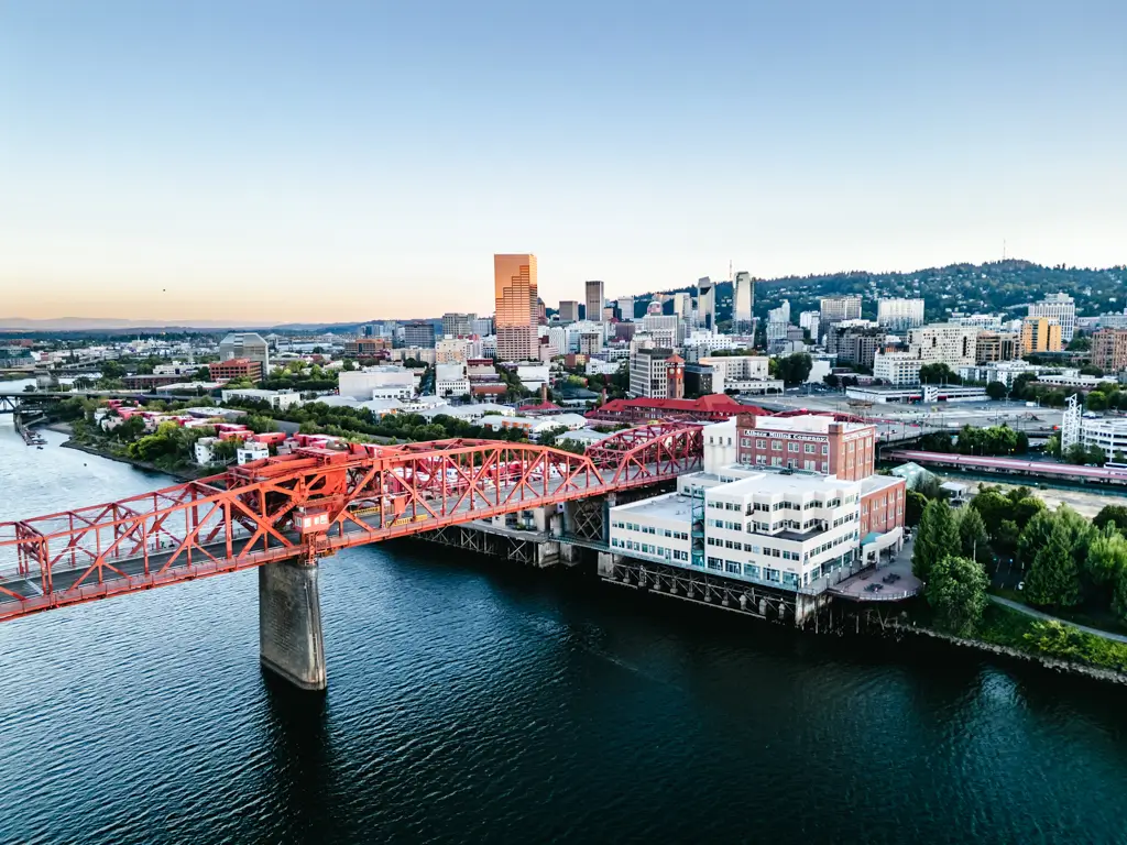 Aerial view of downtown Portland, Oregon, with the red Steel Bridge crossing the Willamette River and the city skyline rising in the background.