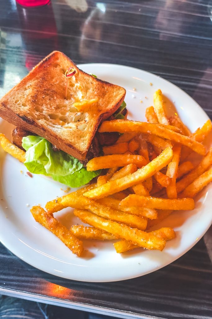 Grilled sandwich with lettuce served alongside crispy seasoned fries on a white plate at a restaurant table