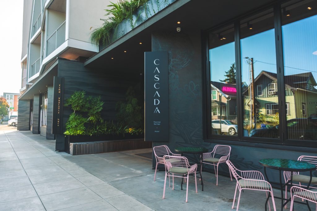 Modern exterior of Cascada Thermal Springs and Hotel with sidewalk café seating and greenery along Alberta Street