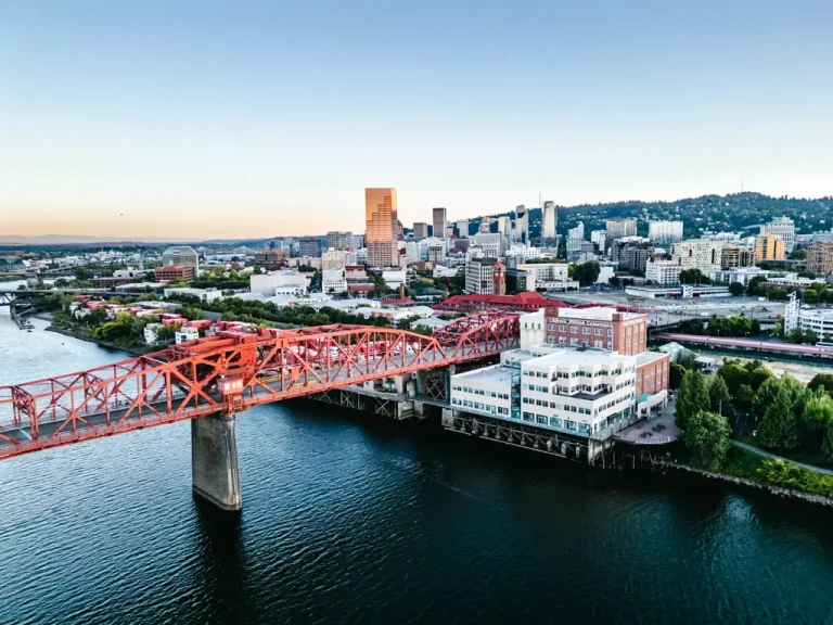 Aerial view of downtown Portland, Oregon, with the red Steel Bridge crossing the Willamette River and the city skyline rising in the background.
