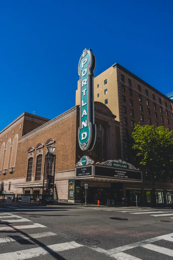 Historic Portland theater building and vertical neon Portland sign in downtown Portland, Oregon, photographed beneath a clear blue sky.
