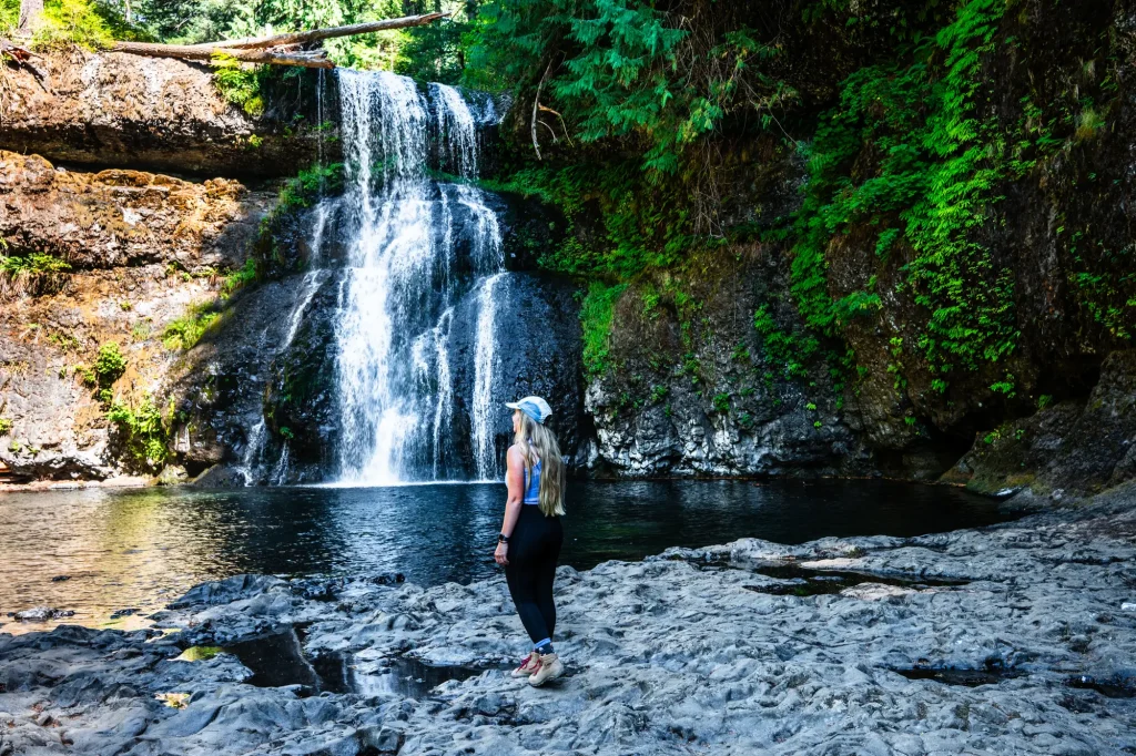 Jordyn Verzera of The Mobile Homie standing beside a forest waterfall and pool along the Trail of Ten Falls at Silver Falls State Park in Oregon.