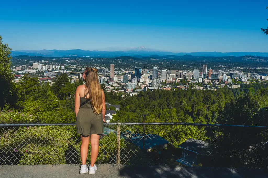 Woman overlooking downtown Portland, Oregon, from Pittock Mansion, with the city skyline, surrounding forests, and Mount Hood visible in the distance.