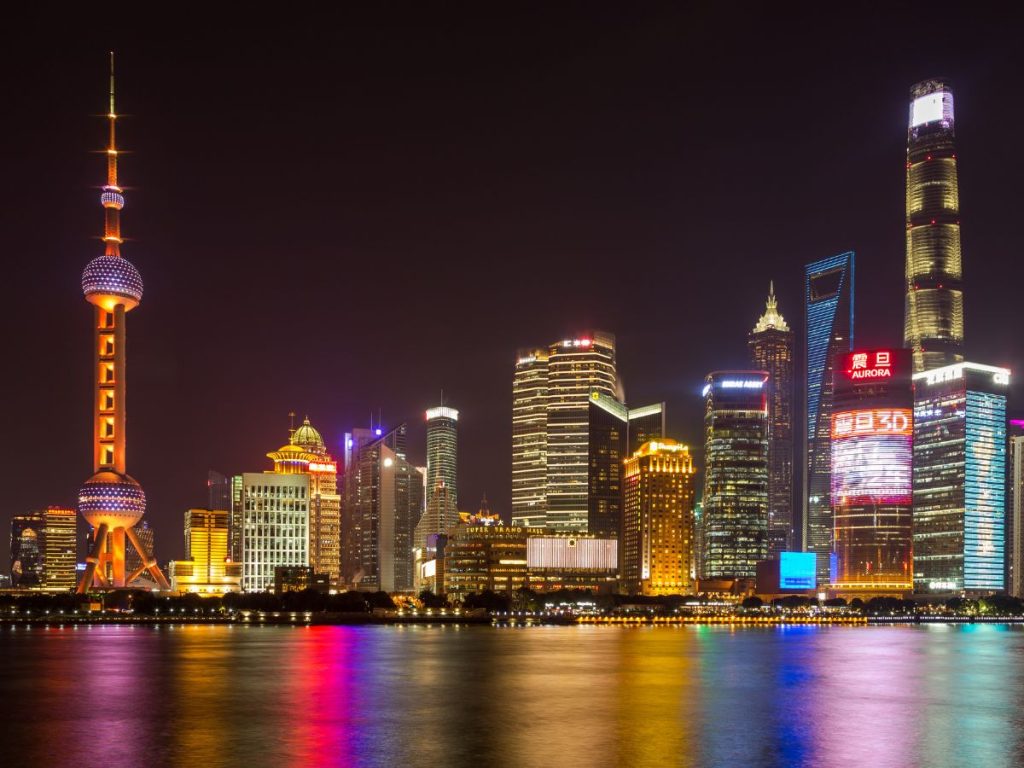 Illuminated skyline of Shanghai at night featuring the Oriental Pearl Tower and modern skyscrapers in Pudong, reflected in the Huangpu River.