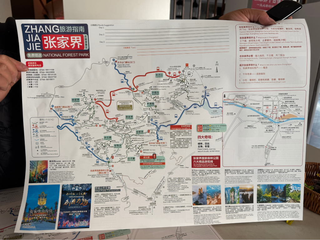A detailed printed tourist map of Zhangjiajie National Forest Park in China, showing scenic areas, bus routes, trails, and major landmarks, held open by two hands.