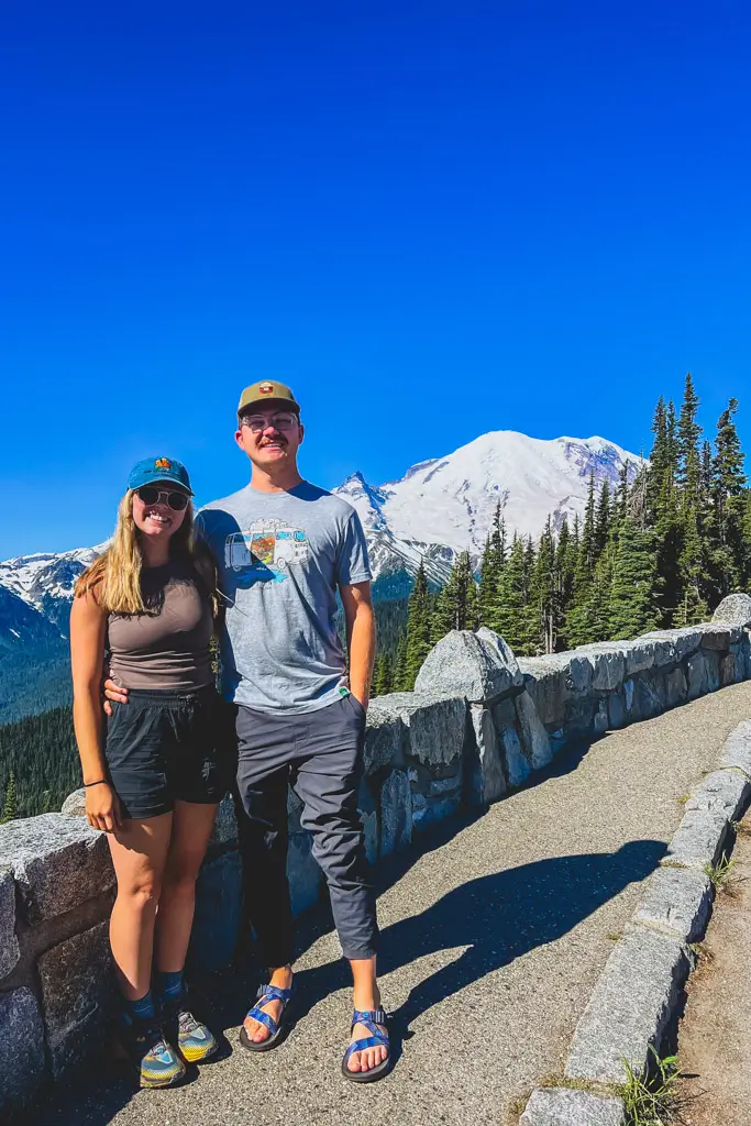 Two travelers stand at the Sunrise overlook with panoramic views of Mount Rainier and the surrounding alpine landscape in Mount Rainier National Park, Washington.