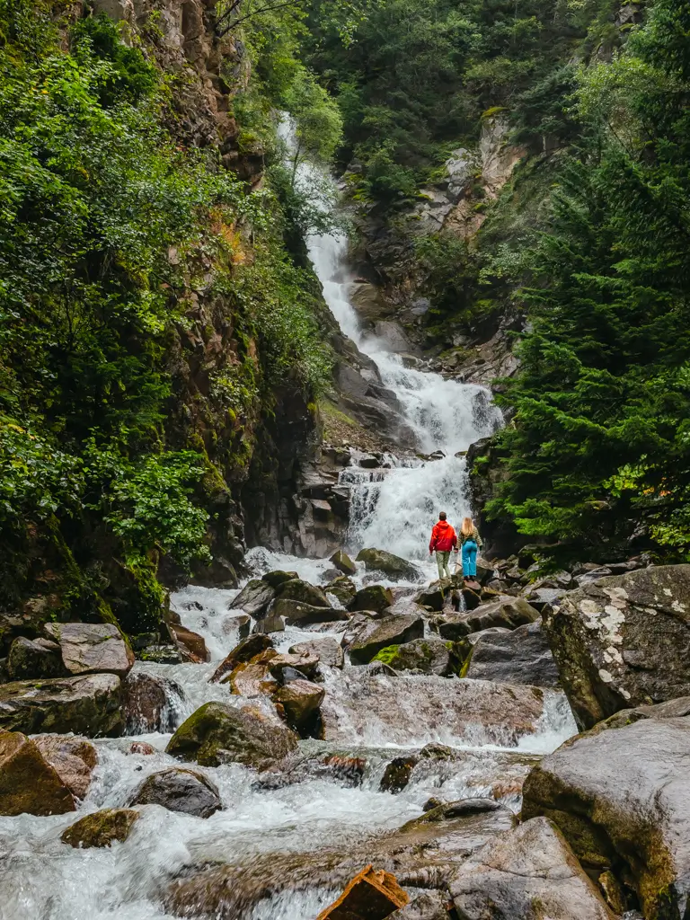 Couple standing on rocks at the base of a cascading waterfall surrounded by lush rainforest in Ketchikan, Alaska.