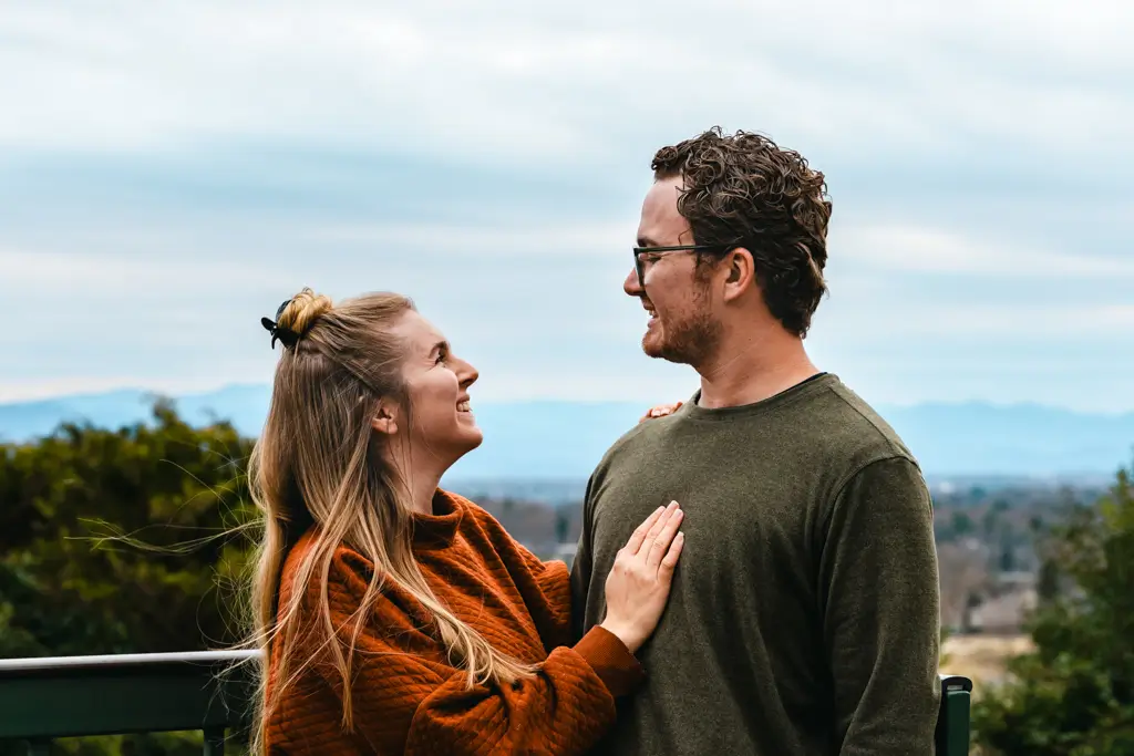 Couple smiling at each other while standing at a scenic overlook with mountain views in the distance during a road trip.