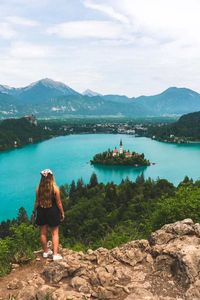 Traveler overlooking the turquoise waters of Lake Bled and Bled Island from the Ojstrica Viewpoint in Slovenia, with the Julian Alps in the background.