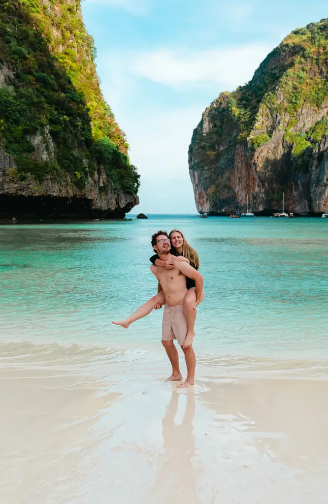 Couple on the white sand beach at Maya Bay in Phi Phi Leh, Thailand, surrounded by turquoise water and towering limestone cliffs.