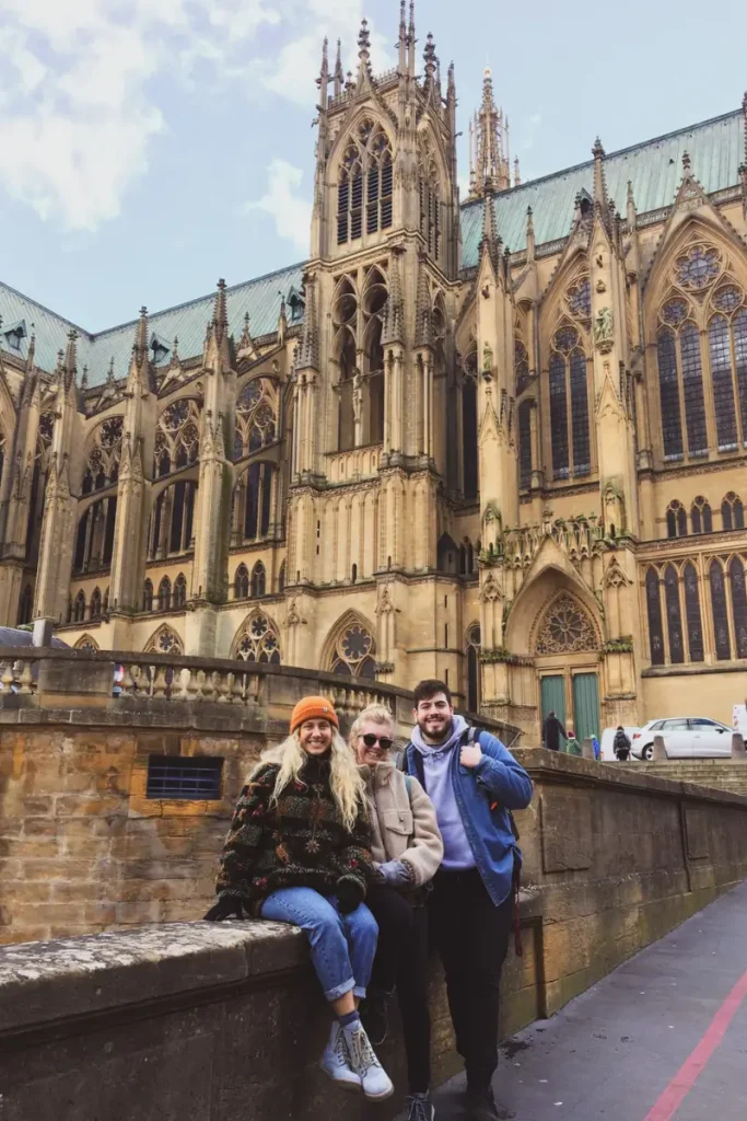 Three travelers posing in front of the Gothic façade of Metz Cathedral in Metz, France, known for its towering architecture and stained-glass windows.