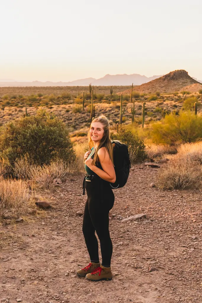 Hiker wearing an Osprey Raptor 10 backpack on a scenic desert trail in Arizona surrounded by saguaro cacti at golden hour.
