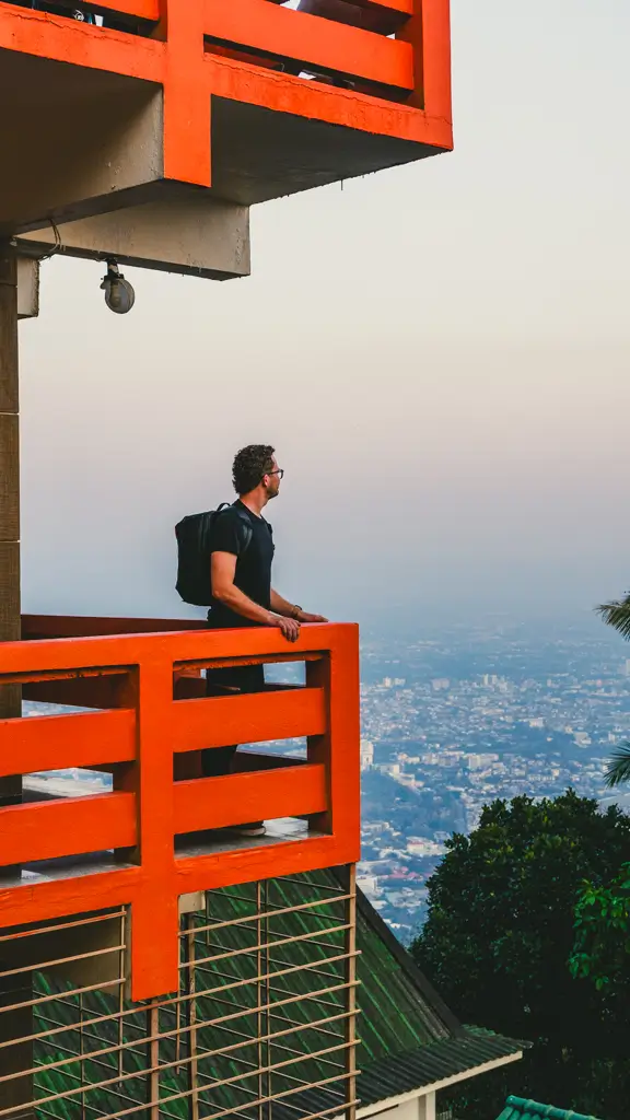 Traveler standing on an orange temple balcony overlooking the city from Wat Phra That Doi Suthep in Chiang Mai, Thailand.