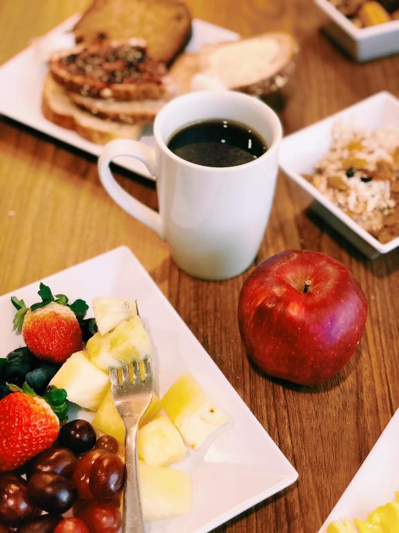 An overhead view of a hotel breakfast spread at the Hyatt Place Seattle Downtown featuring toasted multigrain bread, a white mug of black coffee, a small bowl of granola, a whole red apple, and a plate of fresh strawberries, blueberries, grapes, and pineapple in Seattle, Washington, USA.