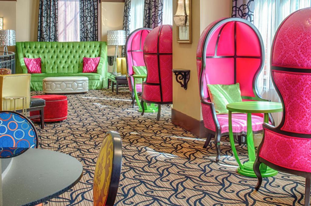 A colorful hotel lounge at Staypineapple, The Maxwell Hotel Seattle Center featuring hot pink dome-back chairs, a tufted green velvet sofa with pink throw pillows, patterned area rugs, mixed-pattern armchairs, and a green side table in Seattle, Washington, USA.