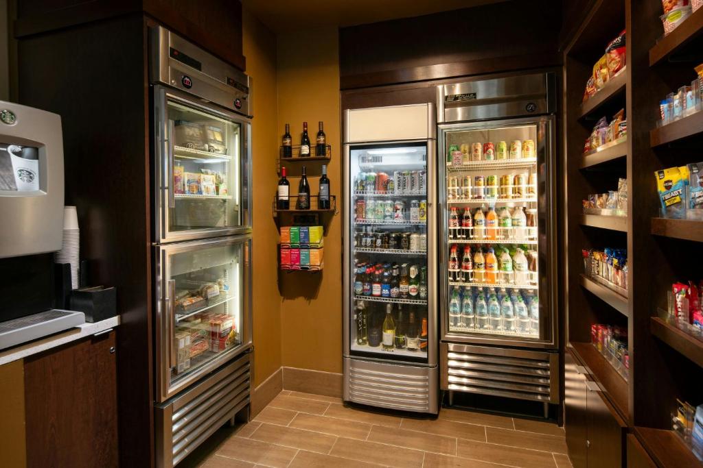 A hotel market and vending area at the Courtyard by Marriott Seattle Downtown Pioneer Square featuring glass-front refrigerators stocked with beverages and snacks, shelves of wine bottles, a Starbucks coffee machine, and packaged snack shelving in Seattle, Washington, USA.