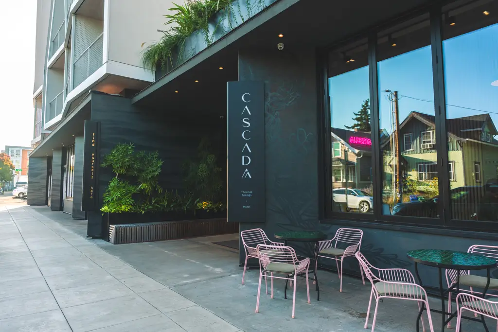 Exterior of Cascada Thermal Springs and Hotel in Portland, Oregon, featuring the modern entrance, greenery, and outdoor seating along the sidewalk.